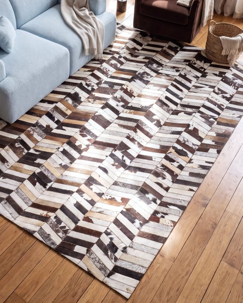Wohnzimmer mit Kuhfellteppich in Fischgrätenmuster auf Holzboden vor einem Sofa