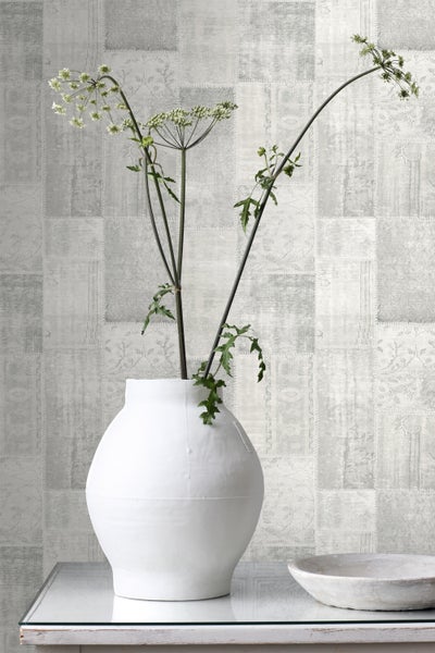 Dekorative Tapete mit Patchworkmuster und Vase mit Pflanze auf dem Tisch