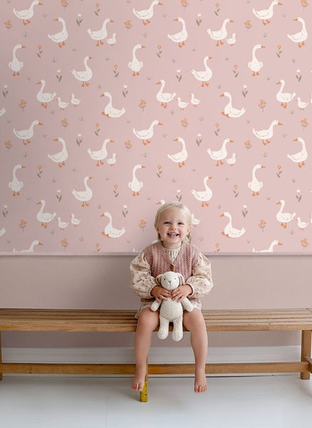 Mädchen sitzt vor einer Wand mit Gänsedekor auf einer Holzbank