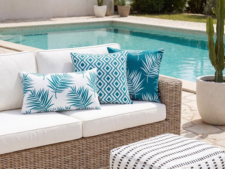 Gartenlounge aus Rattan mit weissen Sitzpolstern und verschiedenen Dekokissen am Poolrand.