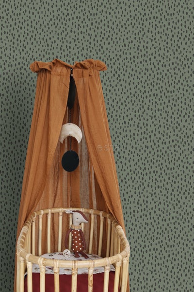 Kinderzimmer-Szene mit Himmelbett, Mobile und Stofftier im Gitterbett vor gemusterter Tapete