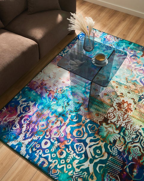 Moderner Wohnbereich mit bunt gemustertem Teppich, einem Glastisch und einem braunen Sofa auf Holzboden.