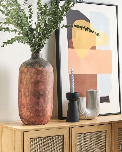 Dekoratives Stillleben auf einem Holzschrank mit Kunstwerk, Kerze und Vasen