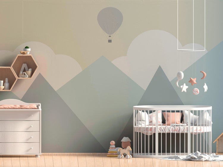 Kinderzimmer mit Vliesfototapete mit Bergen, Wolken und Heißluftballon, weißem Rundbett, Wickelkommode und sechseckigen Wandregalen.