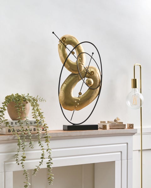 Dekorative goldfarbene Skulptur auf einem Kaminsims mit Zimmerpflanze, Büchern und einem Spiel