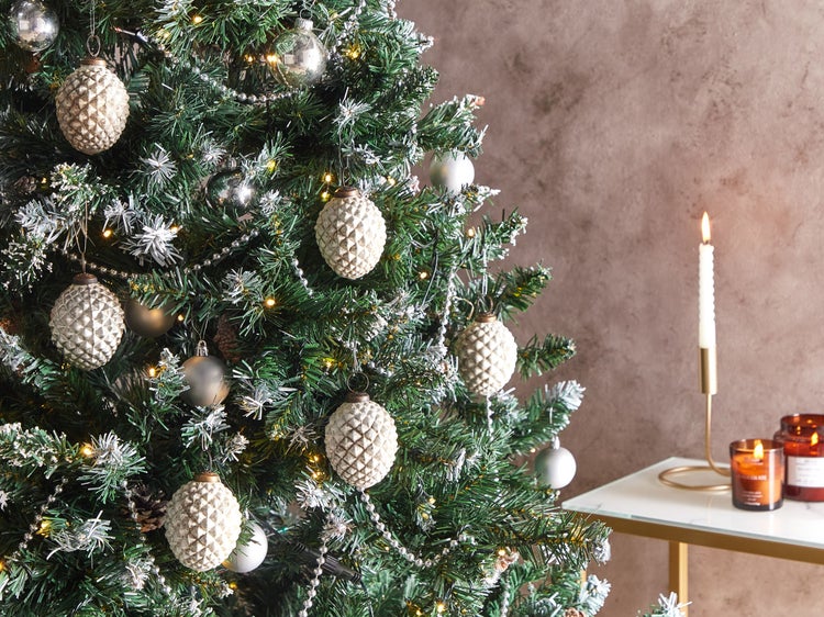 Dekorierter Weihnachtsbaum mit Christbaumkugeln in Zapfenform und Lichterkette neben Tisch mit Kerzen
