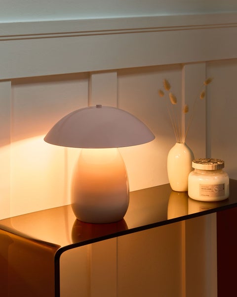 Beleuchtete Tischlampe in Pilzform auf einem gläsernen Konsolentisch neben einer Vase und einer Kerze.