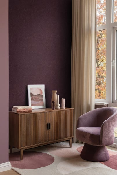 Modernes Wohnzimmer mit dunkelvioletter Mustertapete, Sideboard aus Holz mit vertikalen Lamellen, lila Sessel und gemustertem Teppich.