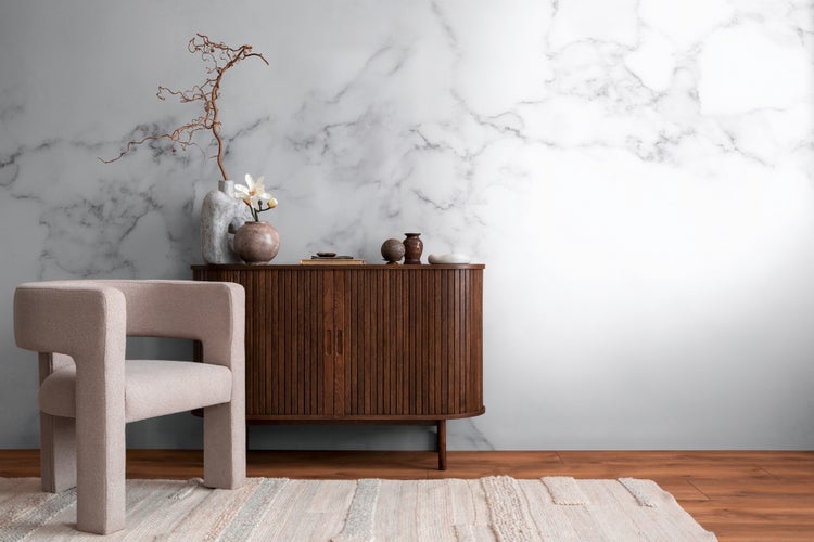Fototapete in Marmoroptik mit grauer Maserung in einem hellen Wohnzimmer mit braunem Sideboard und modernem Sessel.