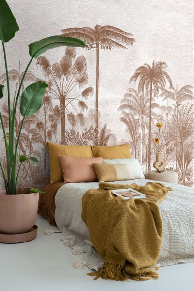 Modernes Schlafzimmer mit einer Fototapete mit Palmenmotiven, einem Bett mit Kissen und Decken sowie einer großen Zimmerpflanze.