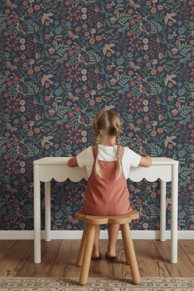 Mädchen sitzt an einem Tisch vor einer Wandtapete mit Blumenmuster