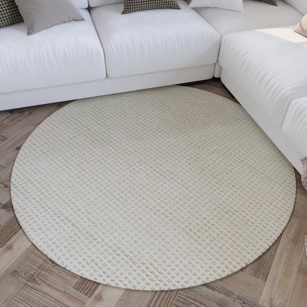 Runder gewebter Teppich mit feiner Textur auf einem Holzfußboden in Fischgrät-Optik neben einem hellen Sofa im Wohnzimmer.