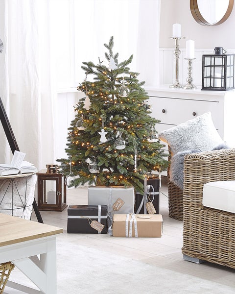 Festlich geschmückter Weihnachtsbaum mit Geschenken in einem hellen Wohnzimmer.