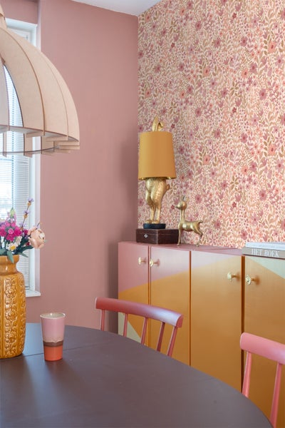 Modern eingerichtetes Zimmer mit floraler Vliestapete, altrosa Wandfarbe und einem farbenfrohen Sideboard mit geometrischem Muster.