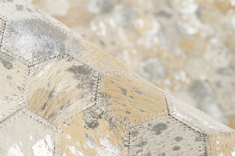 Detailansicht eines Patchwork-Teppichs aus sechseckigen Kuhfell-Elementen mit sichtbaren Nähten und metallischen Effekten.