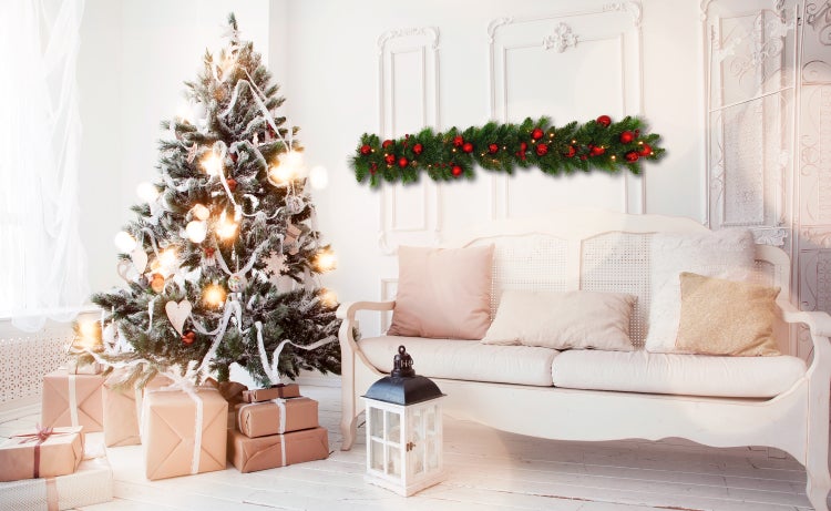 Festlich geschmücktes Wohnzimmer mit Weihnachtsbaum, Geschenken und Tannengirlande über einem Sofa