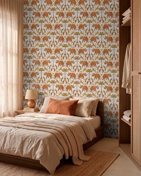 Vliestapete mit Elefanten- und Palmenmuster in einem hellen Schlafzimmer mit Holzbett und Textilien in Naturtönen.