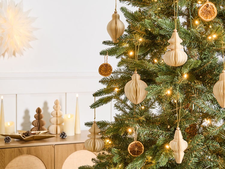 Geschmückter Weihnachtsbaum mit Papieranhängern, getrockneten Orangenscheiben und warmen LED-Lichtern in einem hellen Raum mit Kerzen.