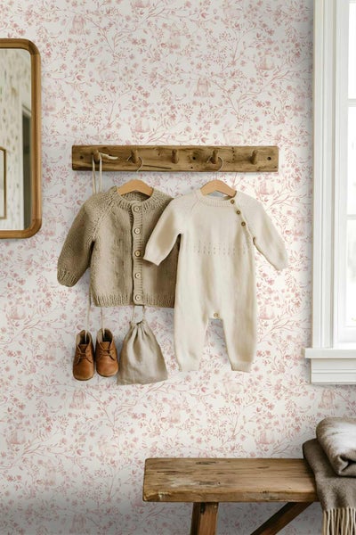 Tapete mit floralem Muster und Hasenmotiven in einem hellen Kinderzimmer mit Garderobe aus Holz und Babykleidung.