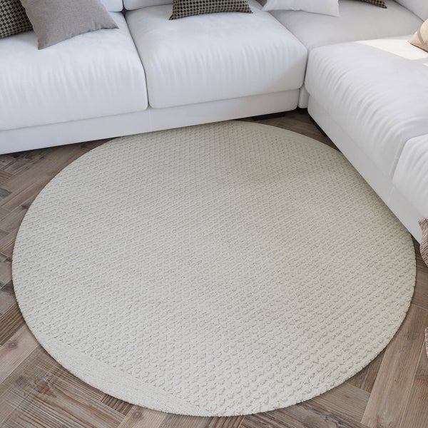 Runder strukturierter Teppich auf hellem Parkettboden vor einem modernen Sofa in einem hellen Wohnzimmer.