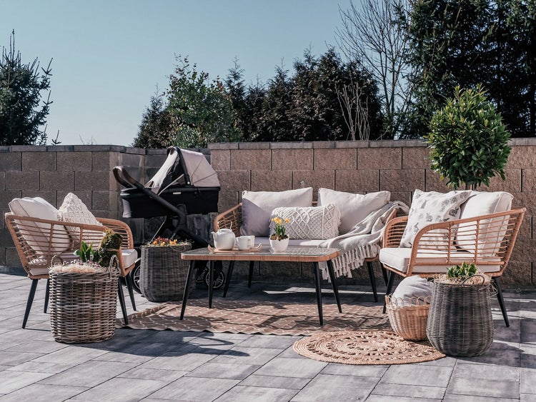 Gartenszene mit Korbmöbeln, Kinderwagen und dekorativen Accessoires für den Außenbereich.