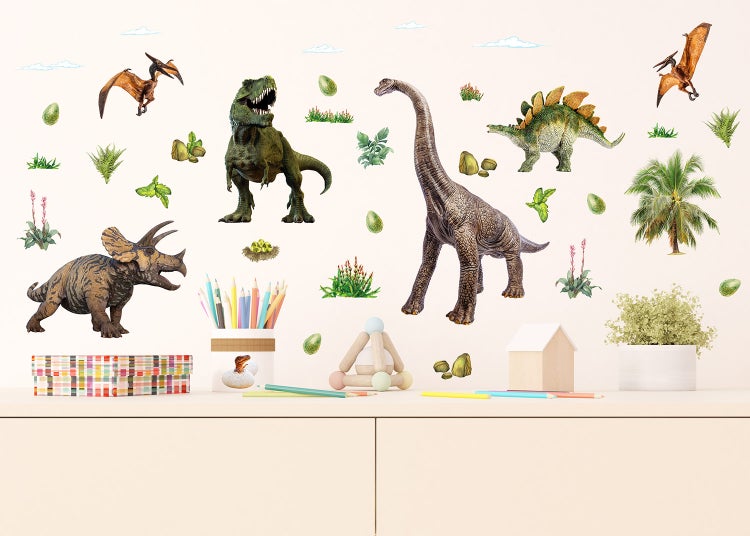 Wandtattoos mit Dinosaurier-Motiven wie T-Rex und Brachiosaurus in einem Kinderzimmer über einer Kommode mit Spielzeug und Stiften.