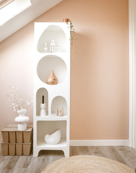 Helles Zimmer mit weißem Regal, dekoriert mit Vasen und Dekoobjekten, vor einer gemusterten Tapete.