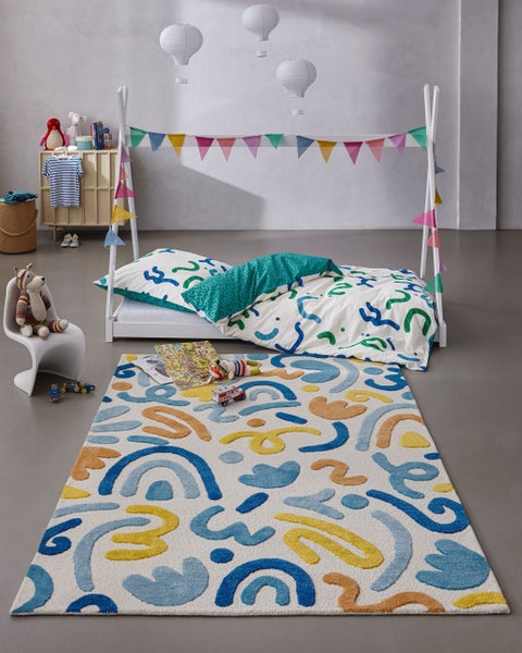 Modernes Kinderzimmer mit einem Hausbett aus Holz, einem Teppich mit abstrakten Mustern, verspielter Bettwäsche und einer bunten Wimpelkette.