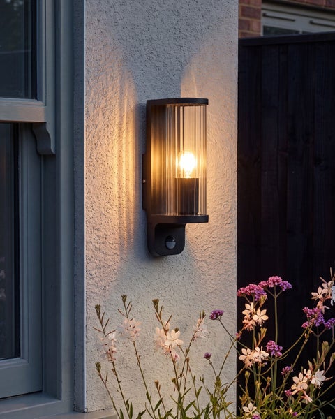 Moderne Außenwandleuchte mit Bewegungsmelder in zylindrischer Form und geriffeltem Glas für die Fassadenbeleuchtung.