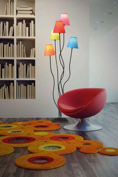 Einrichtungsszene mit Bücherregal, rotem Sessel, Stehlampe mit farbigen Lampenschirmen und Teppich