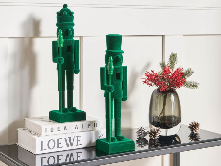 Dekorative grüne Nussknackerfiguren und eine Vase mit Dekozweigen auf einem Tisch