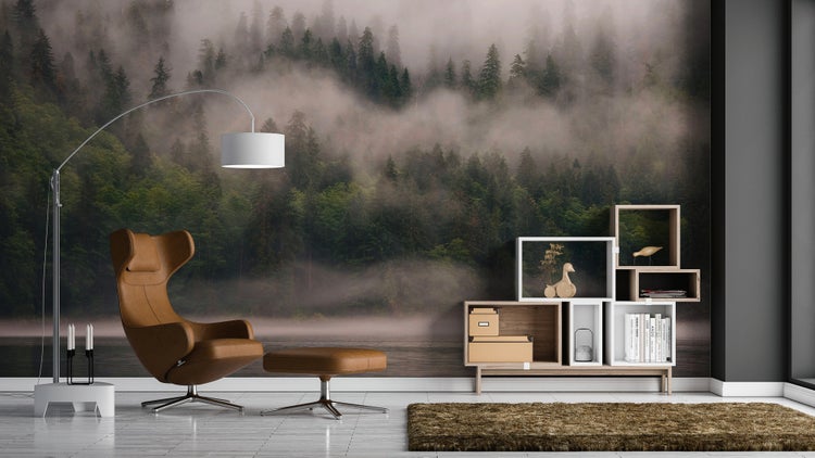 Wohnzimmer mit Fototapete eines nebligen Waldes, einem braunen Ohrensessel aus Leder mit Hocker, modularem Regal und einer Bogenstehleuchte.