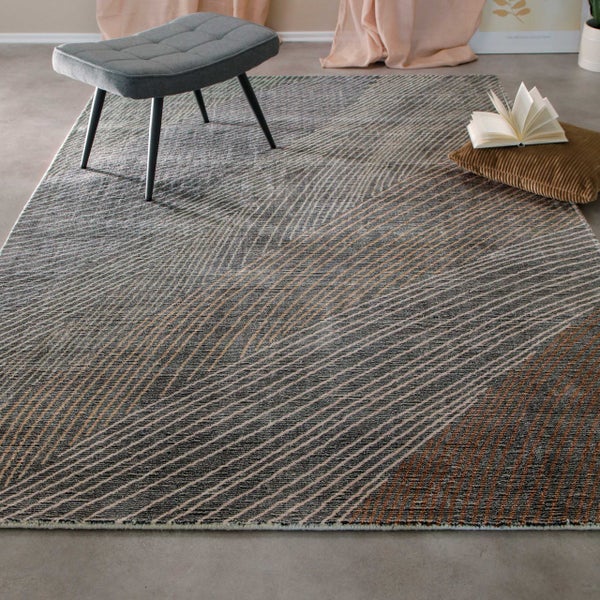Moderner Wohnzimmerteppich mit geometrischem Linienmuster in Grau und Braun, dekoriert mit Polsterhocker und Kissen in einem hellen Raum.