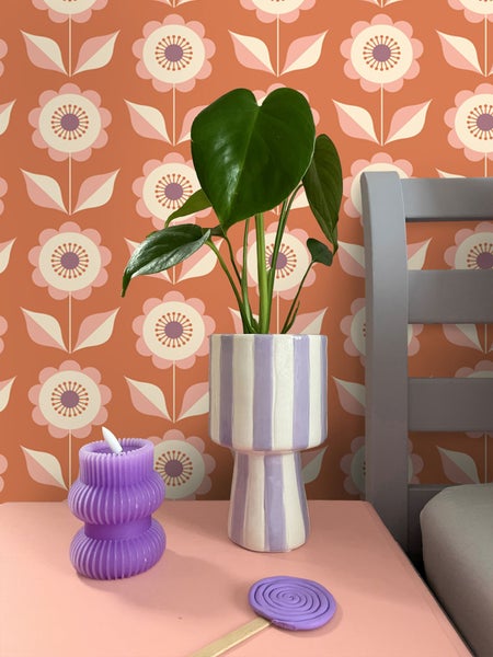 Dekorative Szene mit Zimmerpflanze in gestreiftem Topf, dekorativer Kerze und gewachstem Holzstab auf einem Tisch.