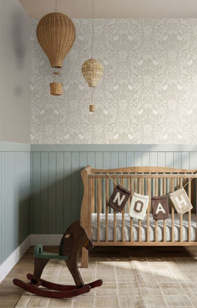 Helles Kinderzimmer mit floral gemusterter Vliestapete, blauen Holzpaneelen, einem Gitterbett aus Naturholz und einem Schaukelpferd.