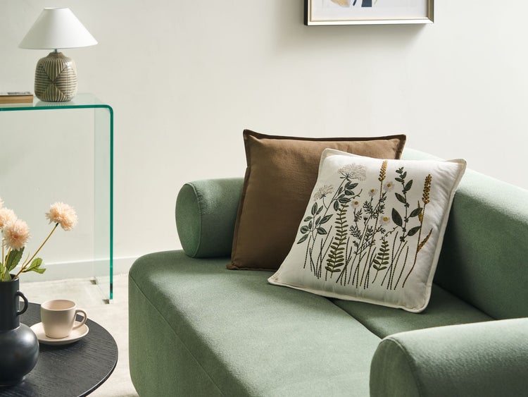 Dekorative Szene mit einem grünen Sofa und zwei Zierkissen, eines mit Blumenmuster.