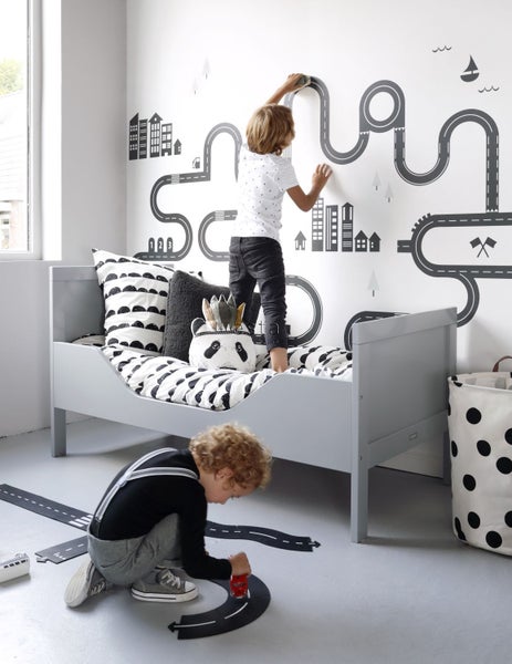 Kinderzimmer mit Bett, Wandaufklebern mit Straßenmotiven und spielenden Kindern