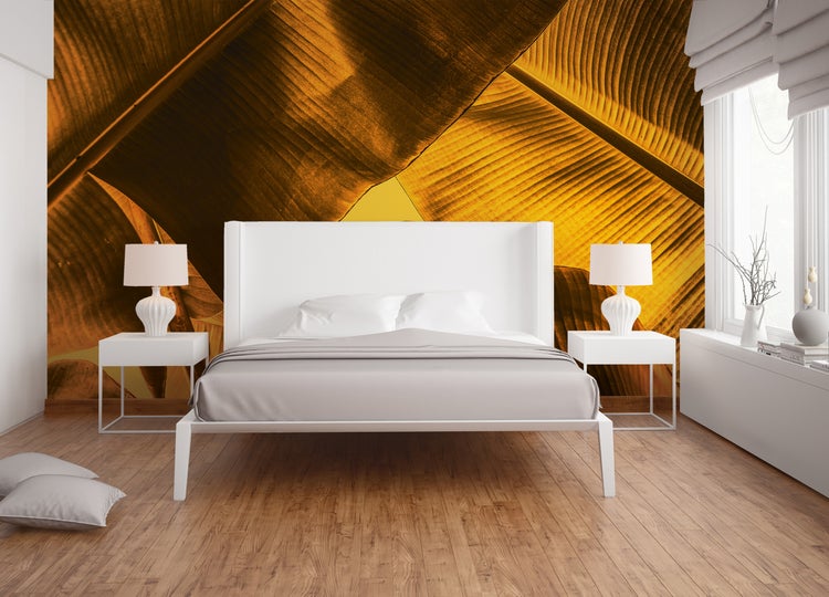 Moderne Fototapete mit goldenen Bananenblättern hinter einem weißen Bett in einem hellen, organisierten Schlafzimmer mit hellem Holzboden.