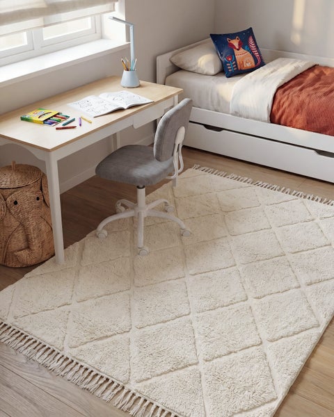 Ein helles Kinderzimmer mit einem strukturierten Teppich mit Rautenmuster, einem Schreibtisch, einem Schreibtischstuhl und einem Kinderbett.