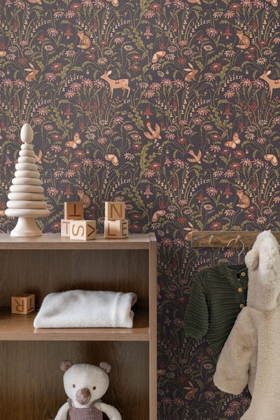 Kindertapete mit Blumenmuster, Rehen und Hasen, neben einem Holzregal mit Spielzeug und einem Kleiderhaken mit Jacken.