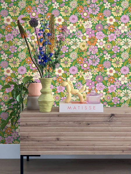 Zimmeransicht mit floraler Tapete, Kommode und Dekorationsgegenständen