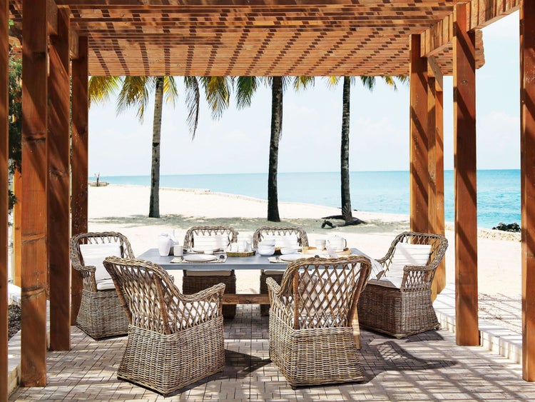 Essbereich mit Gartentisch und Korbstühlen unter einer Holzpergola am Strand