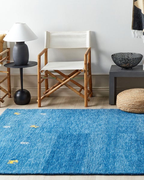 Ein helles Zimmer mit einem blauen Teppich, einem Stuhl mit Holzrahmen und einem Beistelltisch.