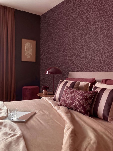 Schlafzimmer mit Tapete im Leopardenmuster, verschiedenen Kissen auf dem Bett und einer modernen Tischleuchte.