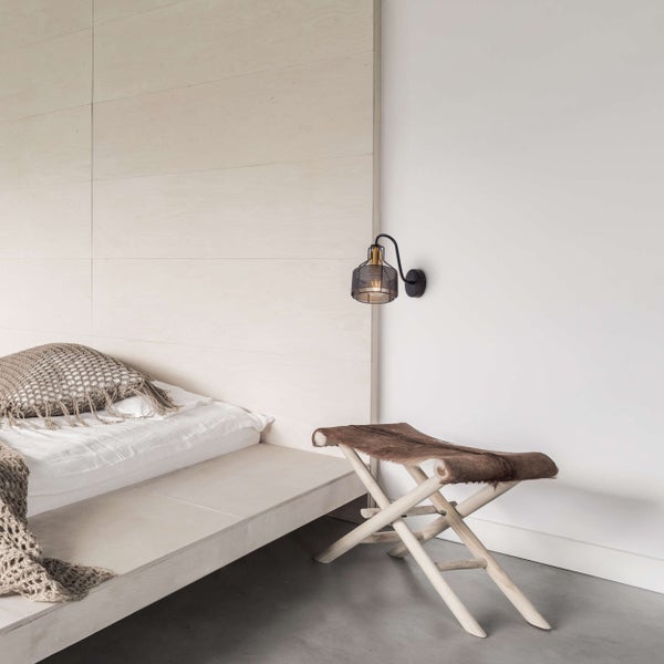 Helles Schlafzimmer mit niedrigem Bett, Wandleuchte und Holzschemel mit Fell