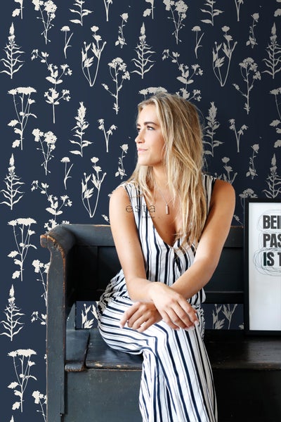 Frau sitzt vor einer dunkelblauen Tapete mit Pflanzenmotiven auf einer Bank