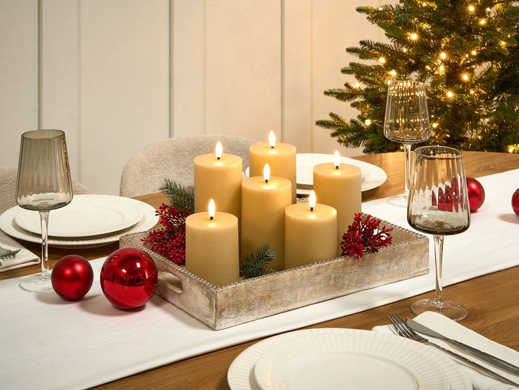 Dekorierter Tisch mit Kerzen, Geschirr und Weihnachtsbaum für festliche Atmosphäre.