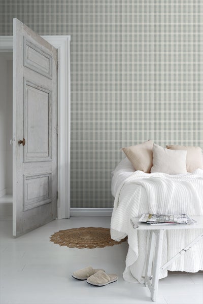 Schlafzimmer mit gemusterter Tapete, Rattan-Kopfteil und Zimmerpflanzen auf einem Nachttisch