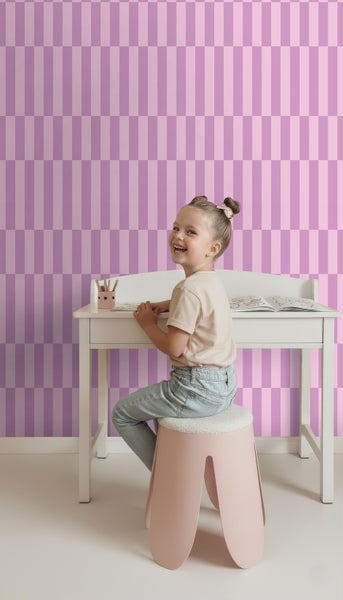Mädchen sitzt an einem Schreibtisch vor einer Wand mit Streifenmuster