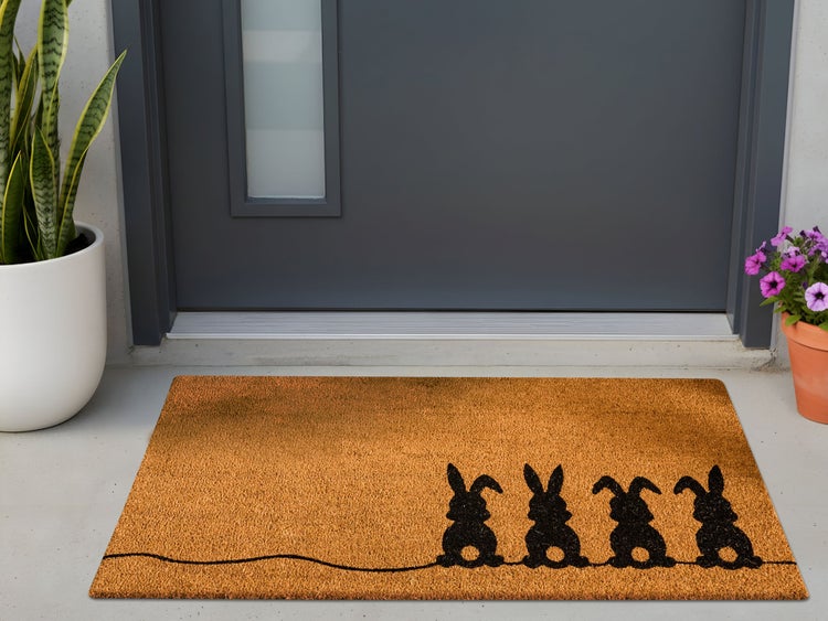 Kokos-Fußmatte mit vier schwarzen Hasen-Silhouetten vor einer grauen Haustür.